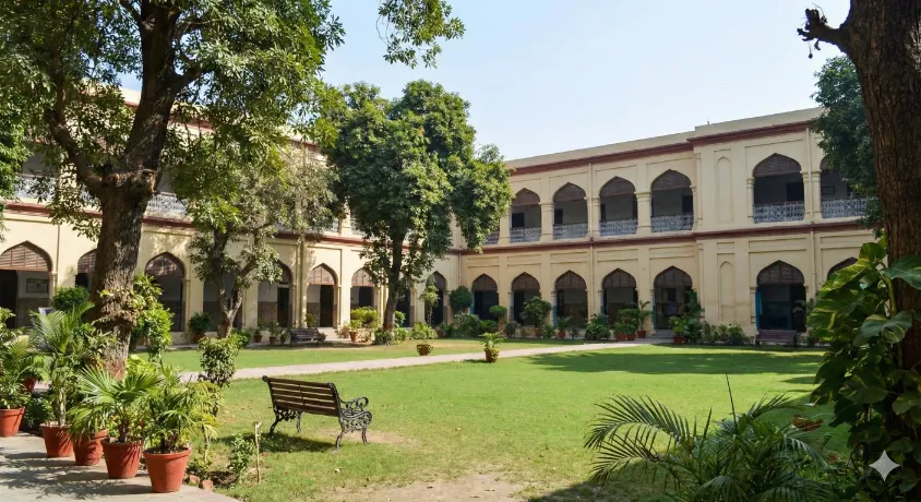 A peaceful, sunny courtyard with green lawns, benches, and historical arched architecture inside the Lahore Presentation Convent School campus.