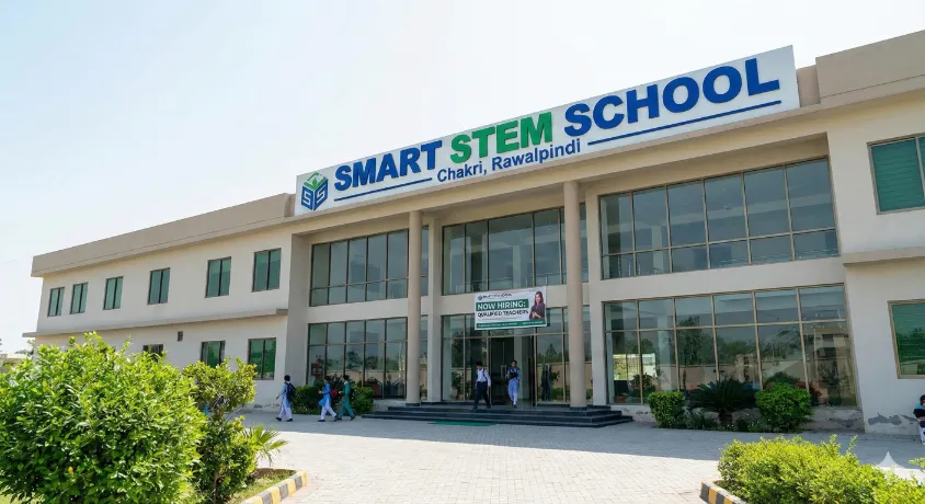 Exterior view of Smart STEM School in Chakri, Rawalpindi, featuring a modern building with a large sign and a 'Now Hiring' banner.
